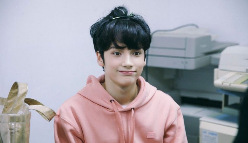 A young man in a pink hoodie sitting in an office.