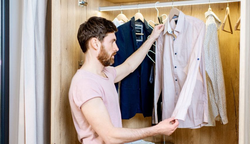 A man is putting on a shirt in a closet.
