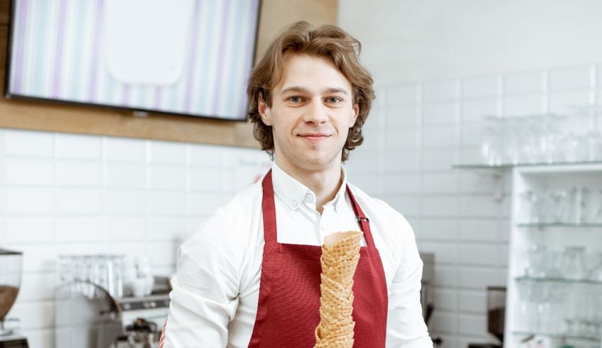 A young man in a red apron holding a doughnut.