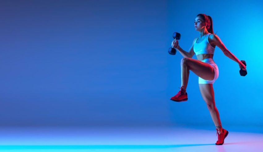 A woman is doing a workout with dumbbells in front of a blue background.