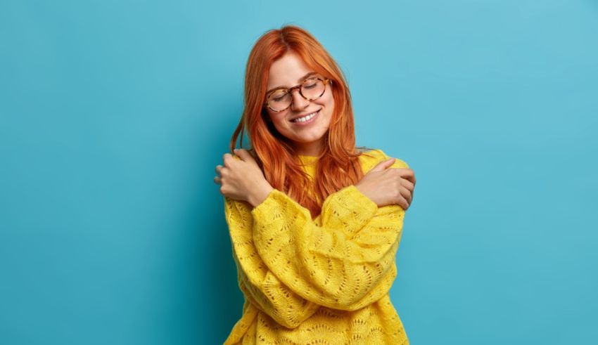 A young woman with red hair and glasses is posing against a blue background.