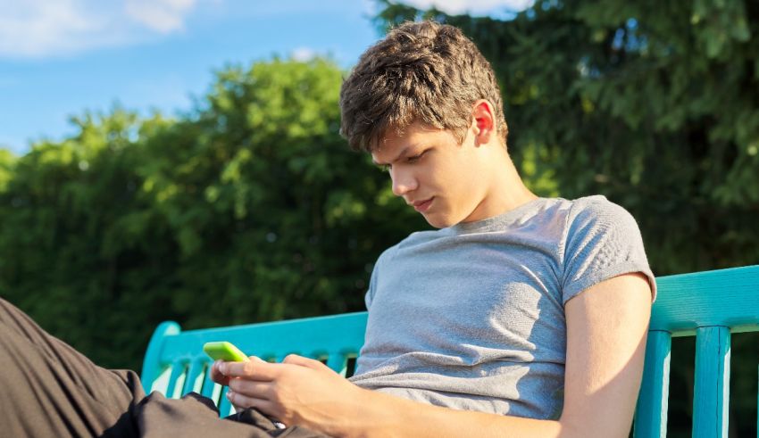 A young man sitting on a bench with a cell phone.