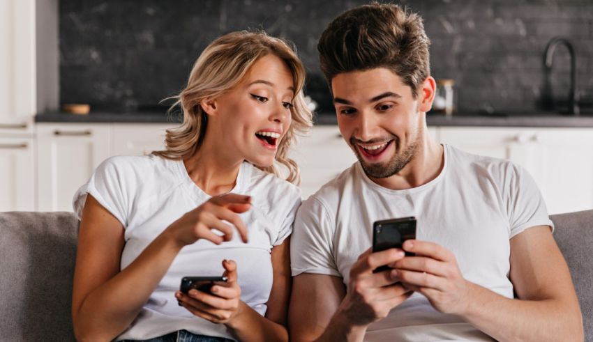 Young man and woman sitting on the couch looking at their cell phone.