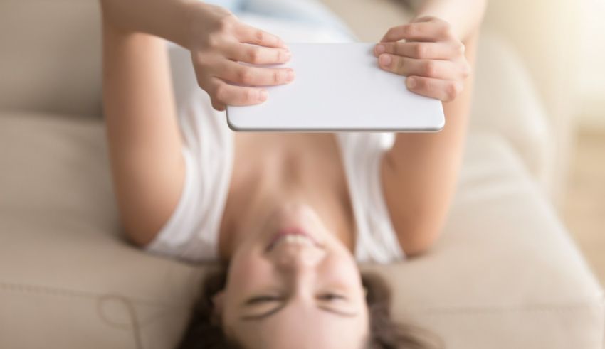 A woman laying on a couch with a tablet in her hand.