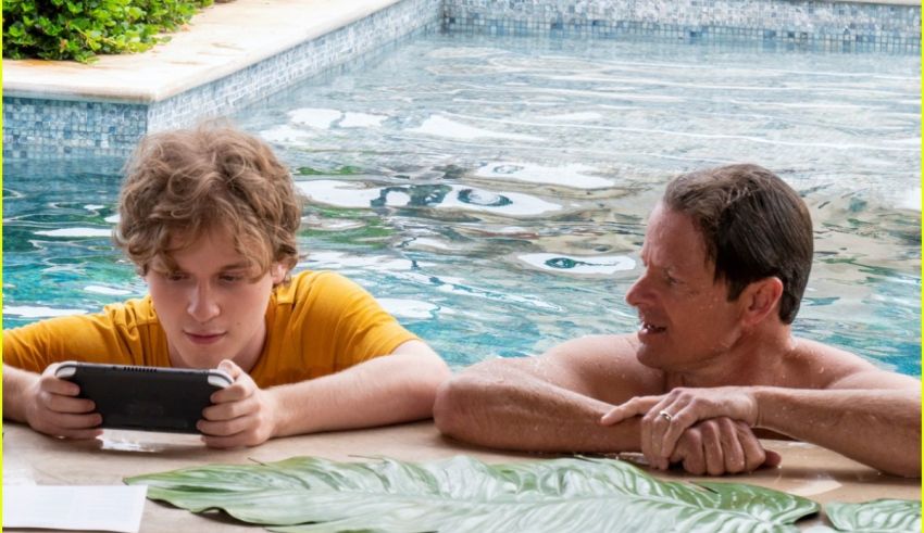 A man and a boy looking at a cell phone by a pool.