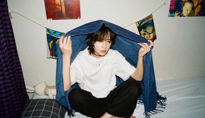 A girl sitting on a bed with a blanket over her head.