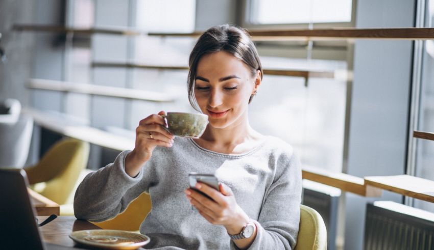 A woman is sitting at a table with a cup of coffee and a cell phone.