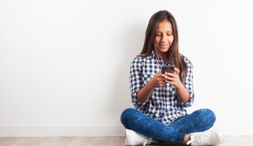 A girl sitting on the floor and using a cell phone.