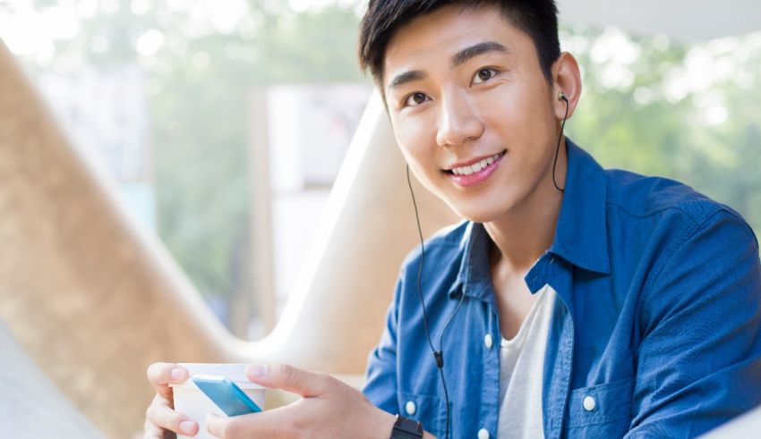 A young asian man holding a phone and listening to music.
