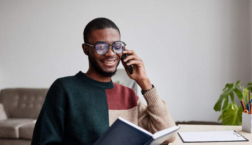 Young african american man in glasses talking on the phone while sitting at a desk.