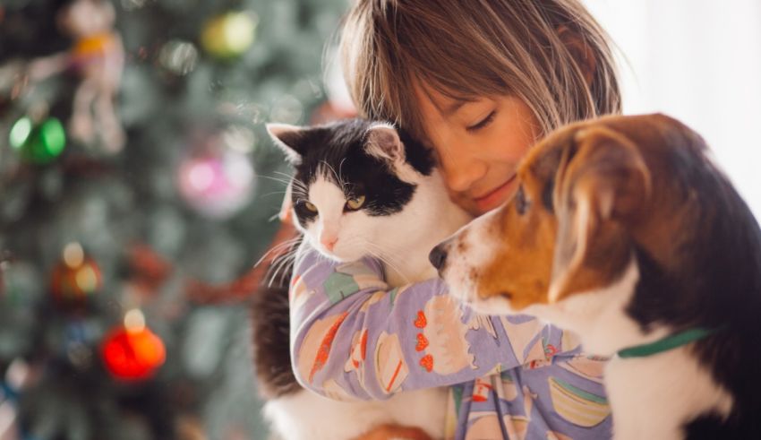 A girl hugging a cat and dog in front of a christmas tree.