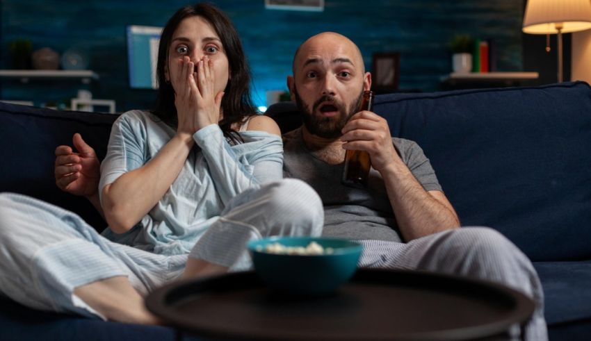 A man and woman are watching a movie on a couch.