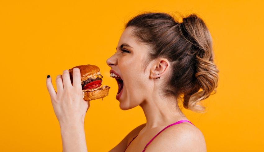 A woman is eating a hamburger on an orange background.