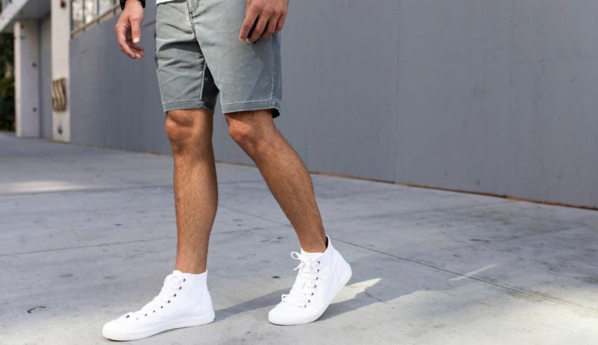 A man in grey shorts and white sneakers standing on a sidewalk.