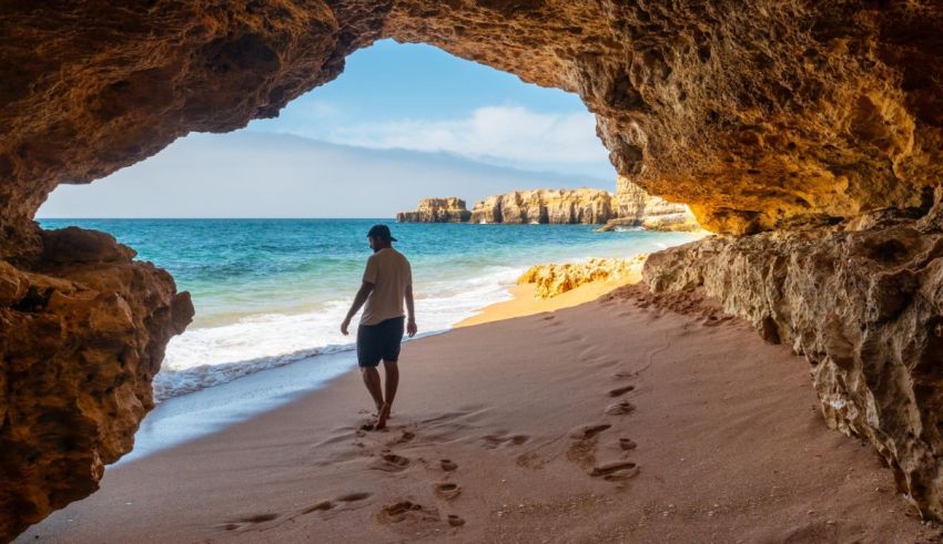 A man walking through a cave on the beach.