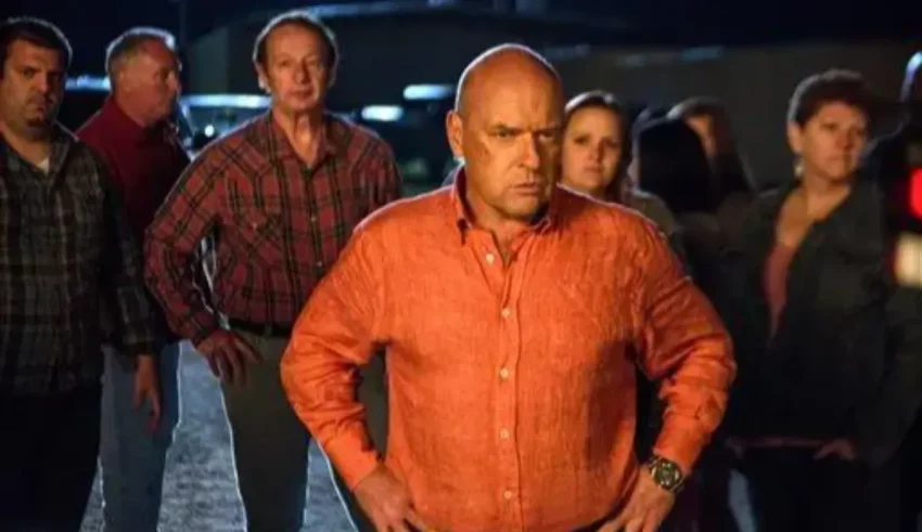 A man in an orange shirt standing in front of a group of people.