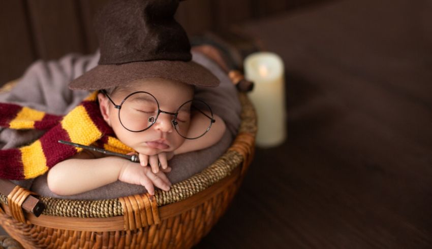 A baby wearing a harry potter hat is sleeping in a basket.