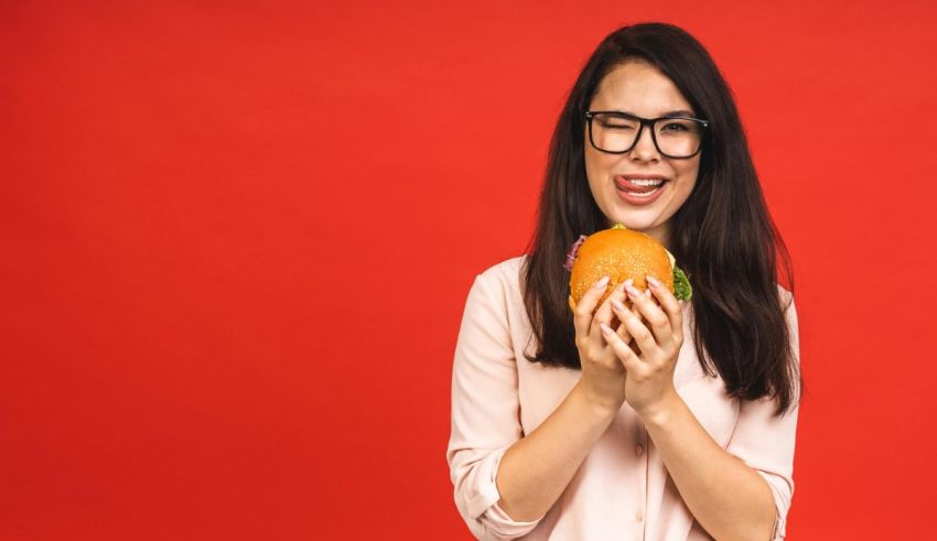 A young asian woman eating a hamburger on a red background.