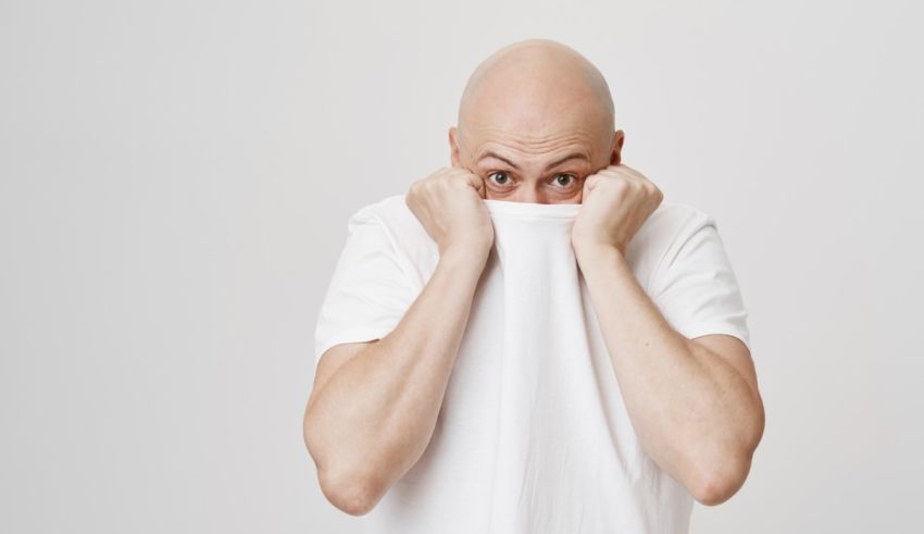 A bald man covering his face with a white t - shirt.