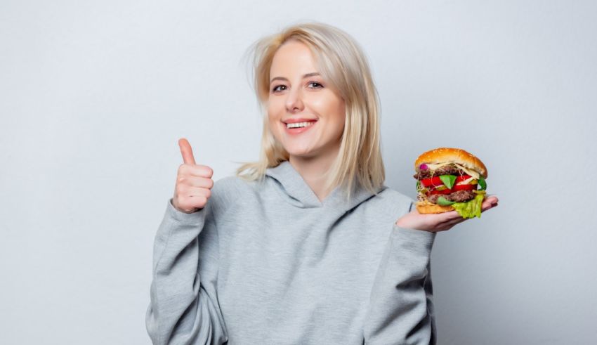 A young woman holding a hamburger and giving thumbs up.