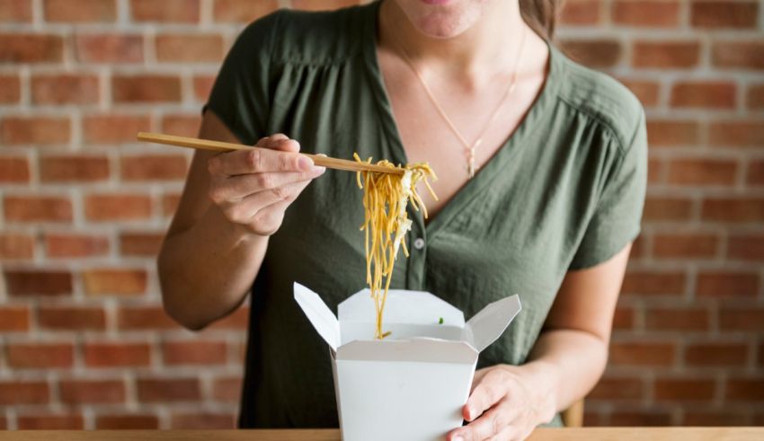 A woman eating noodles in a box with chopsticks.