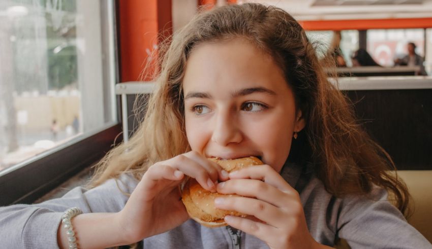A young girl eating a hamburger in a restaurant.