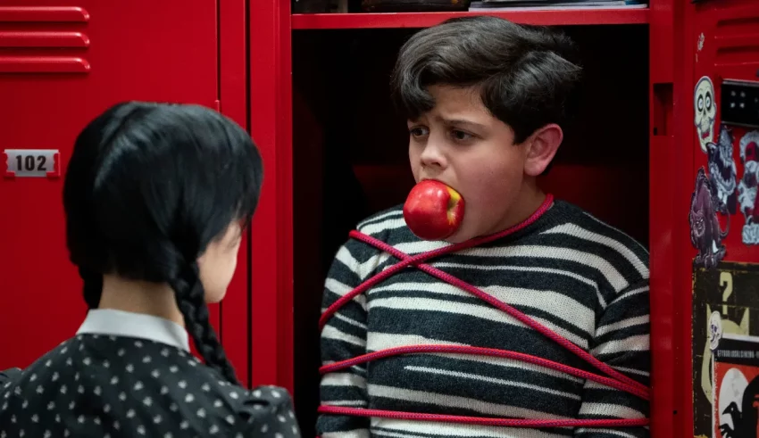 A boy is holding an apple in front of a red locker.