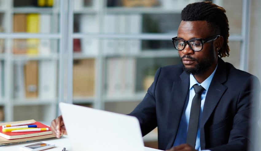 A man in a suit sitting at a desk with a laptop.