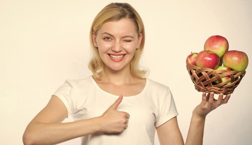 A woman holding a basket of apples and giving a thumbs up.