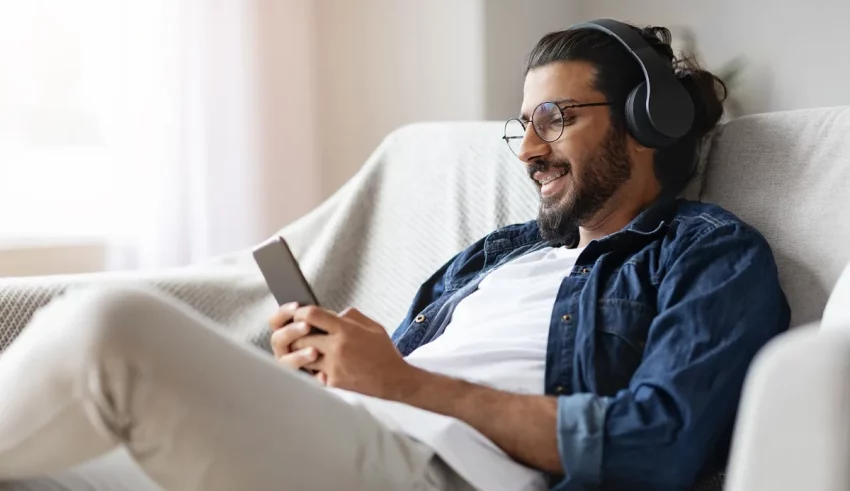 A man wearing headphones is sitting on a couch while listening to music.