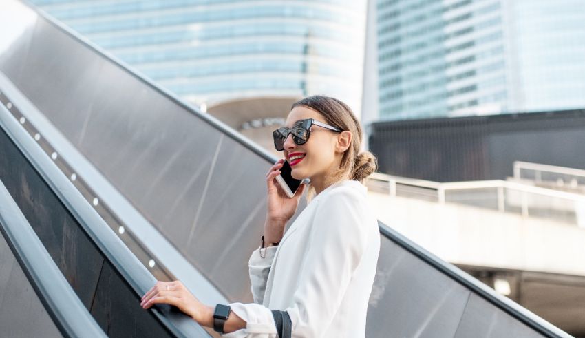 A business woman is talking on the phone while standing on an escalator.