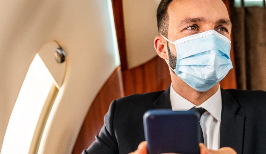 A man in a suit wearing a surgical mask while looking at his phone.