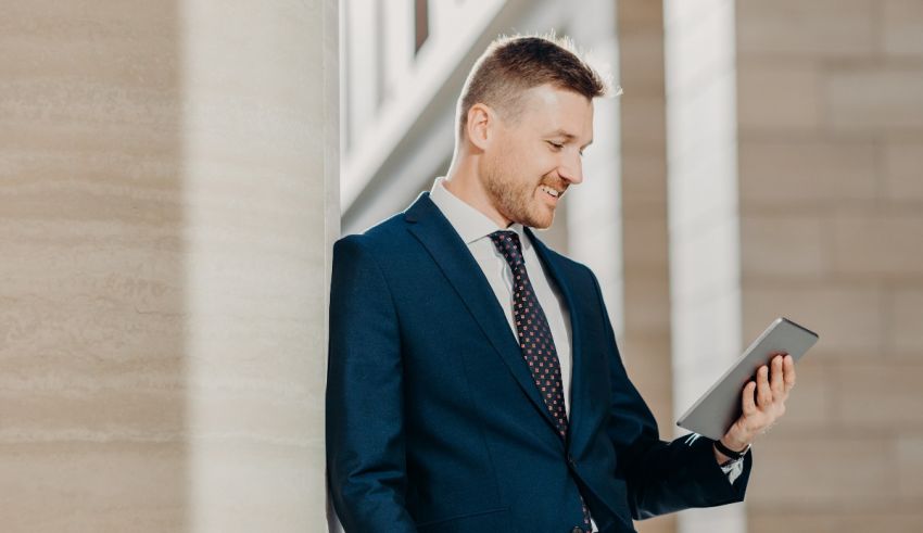 A businessman leaning against a column while using a tablet computer.