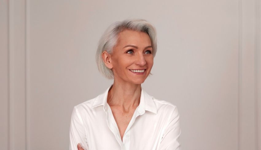 A woman with gray hair is smiling in a white shirt.