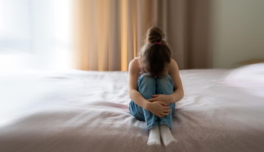 A little girl sitting on a bed with her hands on her knees.