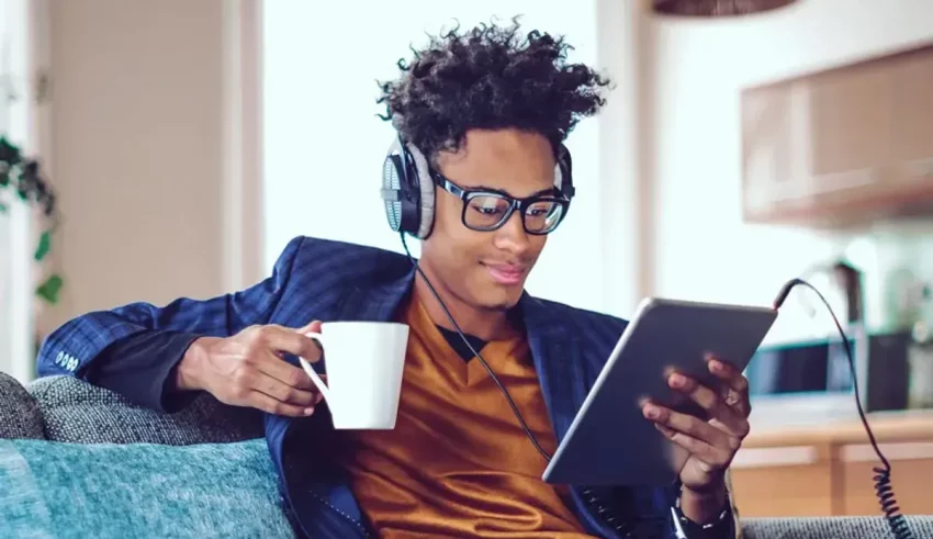A young man listening to music while sitting on a couch with a cup of coffee.