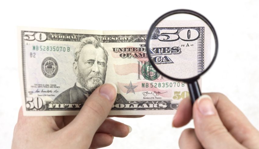 A person holding a magnifying glass over a 50 dollar bill.