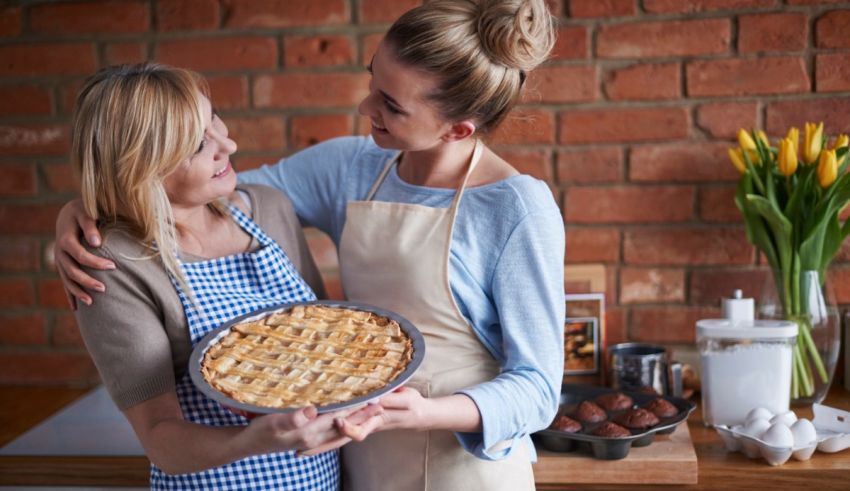 Two women in aprons holding pies in the kitchen.
