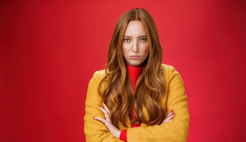 A young woman with red hair is posing on a red background.