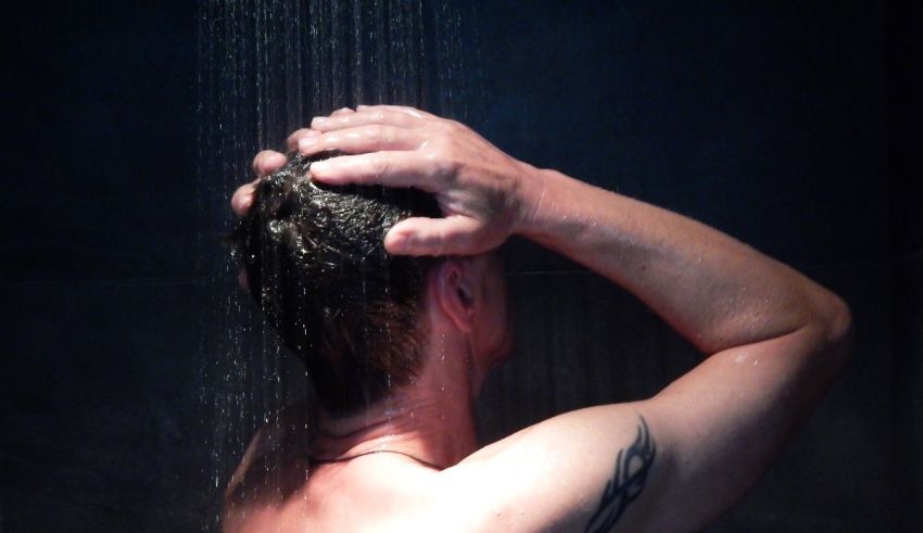 A man taking a shower with a tattoo on his head.