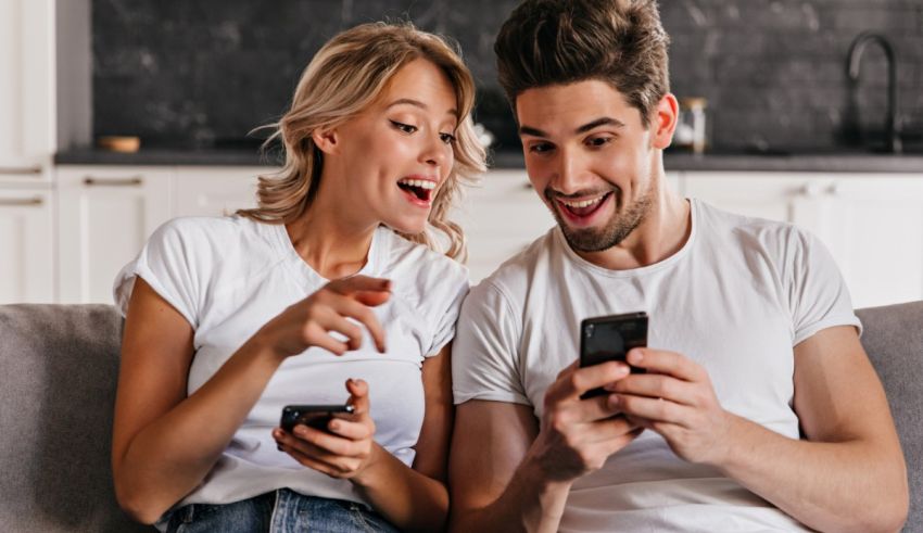 A young man and woman are sitting on a couch and looking at their cell phones.