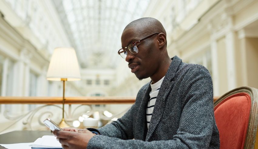 A man in glasses sitting at a table with a cell phone.