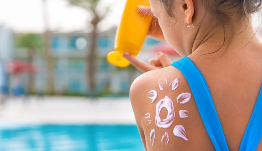 A girl is applying sunscreen to her back near a swimming pool.