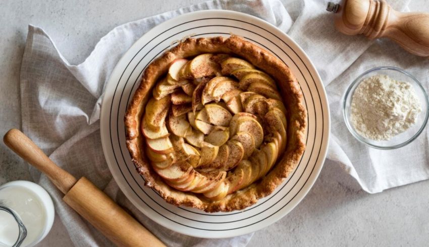 An apple pie on a plate next to a rolling pin.