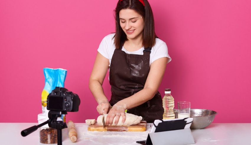 A woman in an apron is kneading dough in front of a camera.