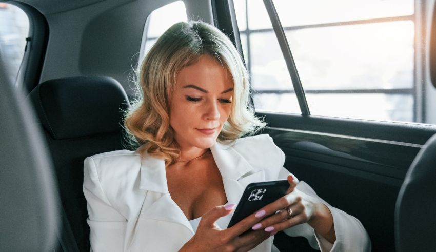 A woman is sitting in the back seat of a car looking at her phone.