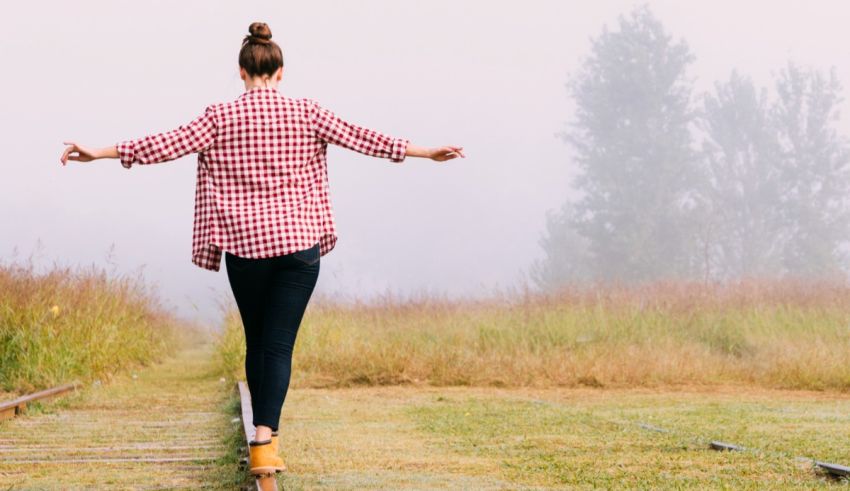 A woman is standing on a train track with her arms outstretched.