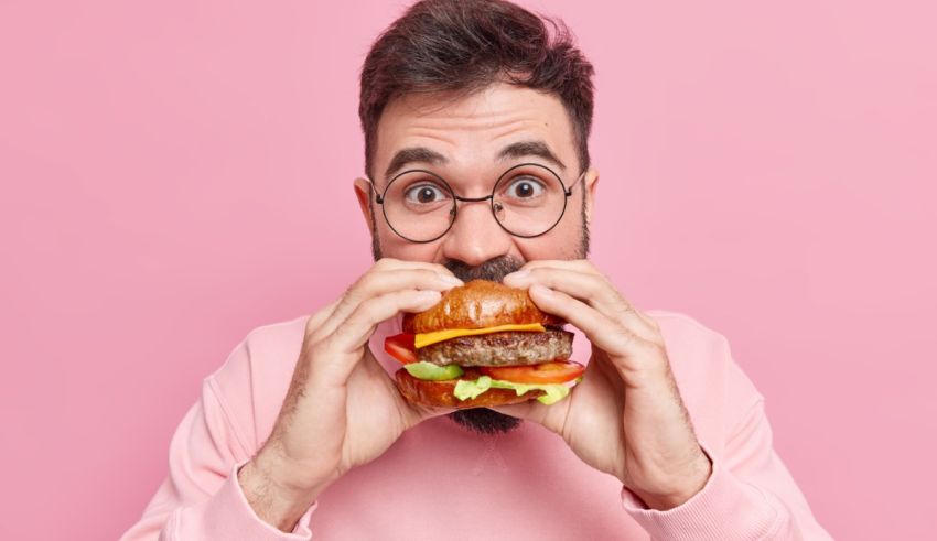 A man with glasses is eating a hamburger on pink background.