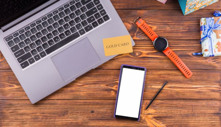 A laptop, cell phone, watch and gifts on a wooden table.