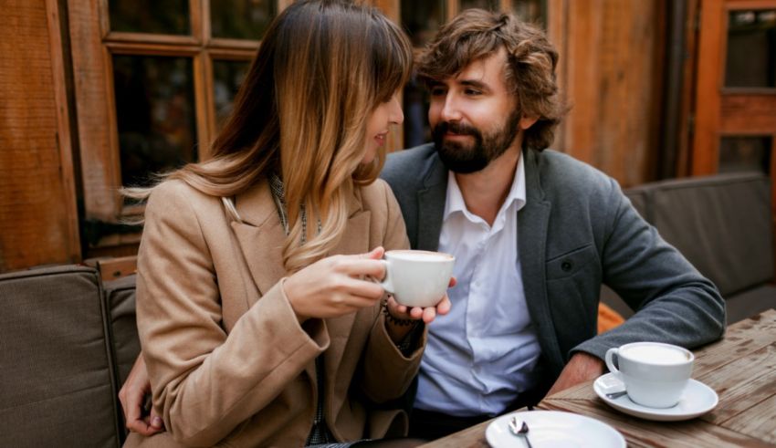 A man and woman are sitting at a table and drinking coffee.